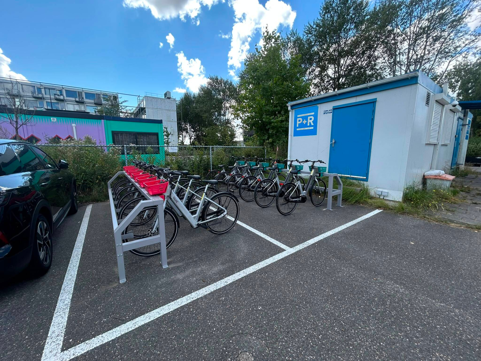 Overzicht van het fietsenrek met gewone fietsen en e-bikes naast geparkeerde auto's